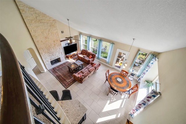 living room with ceiling fan, tile patterned flooring, high vaulted ceiling, a textured ceiling, and a stone fireplace