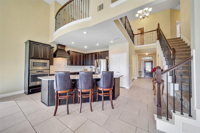 kitchen featuring a breakfast bar, premium range hood, stainless steel appliances, dark brown cabinetry, and an island with sink