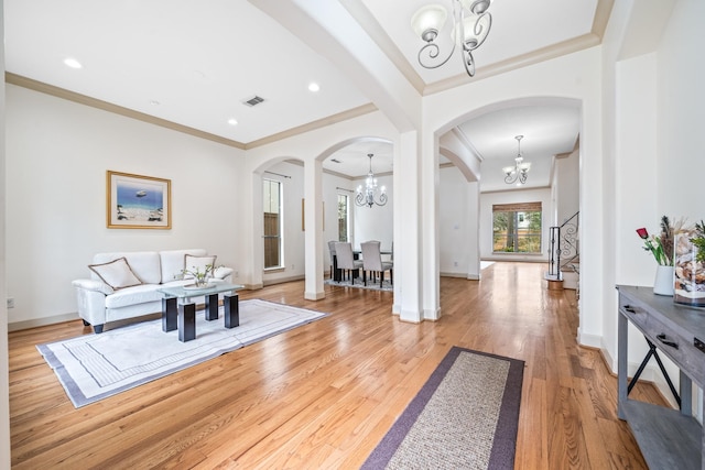 living area featuring arched walkways, a notable chandelier, visible vents, ornamental molding, and light wood-type flooring