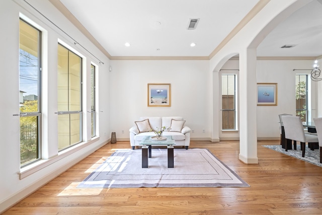 living area featuring light wood-type flooring, arched walkways, visible vents, and ornamental molding