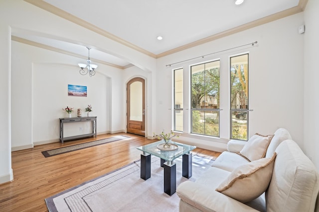 living area featuring arched walkways, a chandelier, wood finished floors, and ornamental molding