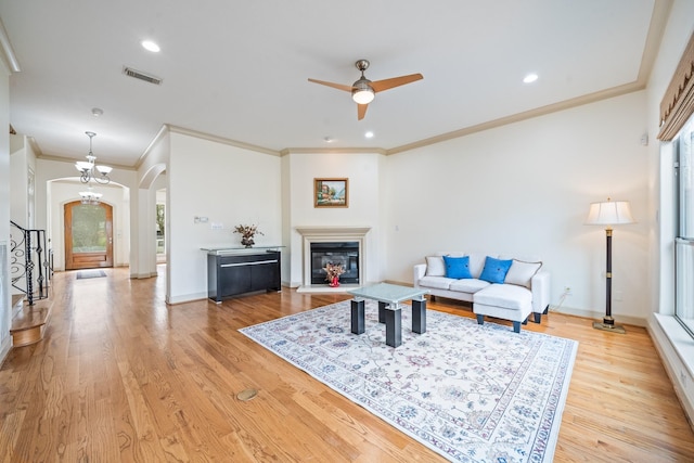 living room featuring arched walkways, visible vents, baseboards, light wood finished floors, and a glass covered fireplace