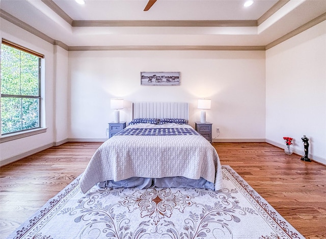 bedroom featuring a tray ceiling, crown molding, ceiling fan, wood finished floors, and baseboards