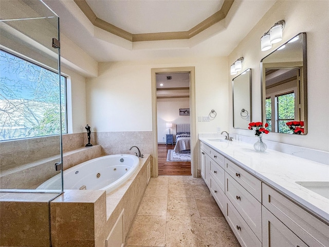 ensuite bathroom featuring a sink, a raised ceiling, double vanity, a tub with jets, and ensuite bath