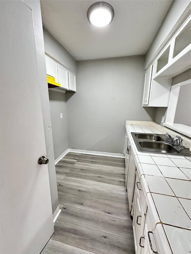 kitchen with light hardwood / wood-style flooring, sink, tile counters, and white cabinets