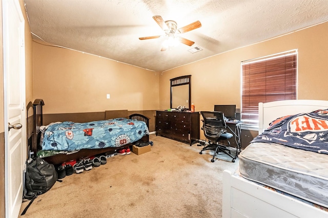 bedroom with ceiling fan, light colored carpet, and a textured ceiling