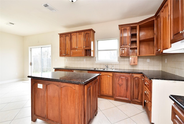 kitchen with sink, a center island, light tile patterned floors, dark stone counters, and decorative backsplash