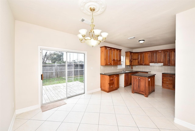 kitchen with pendant lighting, sink, decorative backsplash, a center island, and a notable chandelier