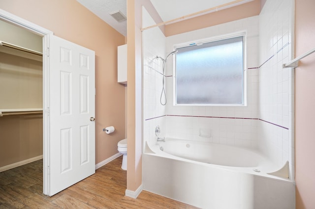 bathroom with hardwood / wood-style floors, tiled shower / bath, and toilet