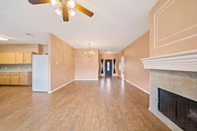 unfurnished living room with ceiling fan with notable chandelier and light hardwood / wood-style flooring