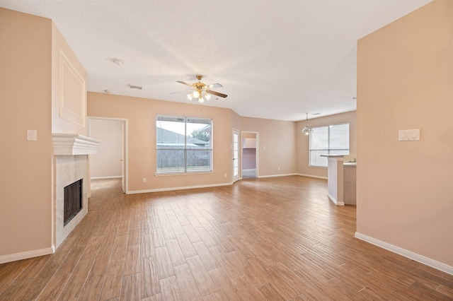 unfurnished living room featuring plenty of natural light, ceiling fan with notable chandelier, and light hardwood / wood-style flooring