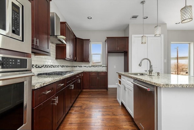 kitchen featuring sink, appliances with stainless steel finishes, light stone countertops, decorative light fixtures, and wall chimney exhaust hood