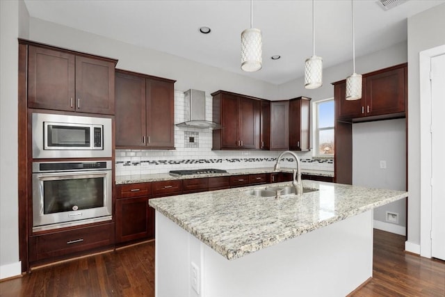 kitchen with wall chimney exhaust hood, sink, hanging light fixtures, an island with sink, and stainless steel appliances