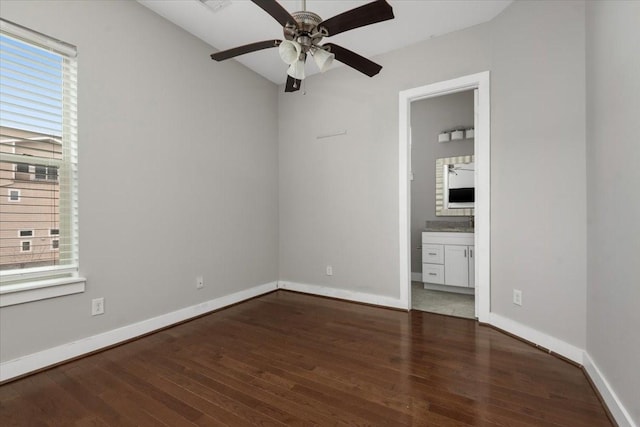 unfurnished bedroom featuring dark hardwood / wood-style flooring, ensuite bath, multiple windows, and ceiling fan