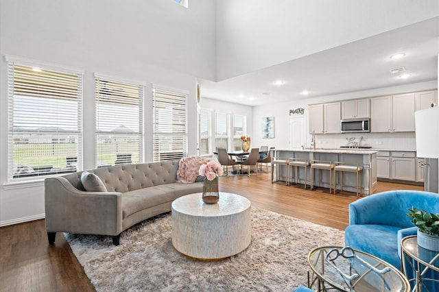 living room with sink, light hardwood / wood-style flooring, and a high ceiling