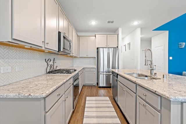 kitchen featuring sink, hardwood / wood-style flooring, appliances with stainless steel finishes, gray cabinetry, and an island with sink