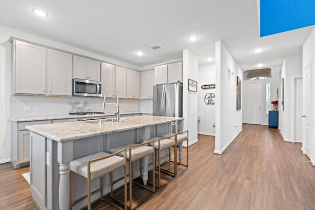 kitchen with appliances with stainless steel finishes, sink, a kitchen bar, a kitchen island with sink, and light stone counters