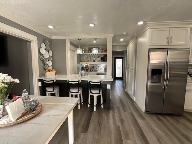 kitchen with pendant lighting, an island with sink, a breakfast bar area, stainless steel fridge, and light stone counters