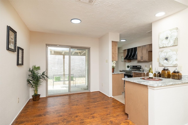 kitchen featuring dark hardwood / wood-style floors, kitchen peninsula, wall chimney range hood, a textured ceiling, and electric stove