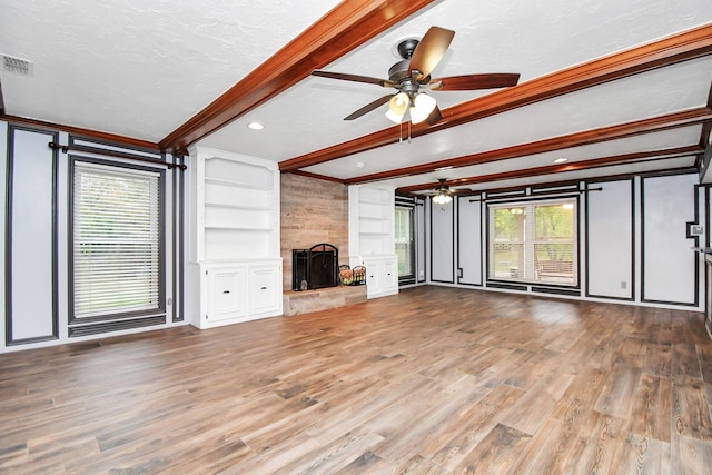 unfurnished living room with hardwood / wood-style floors, a fireplace, a textured ceiling, built in shelves, and beamed ceiling