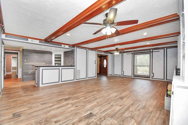 unfurnished living room featuring ceiling fan, a textured ceiling, beamed ceiling, and light wood-type flooring