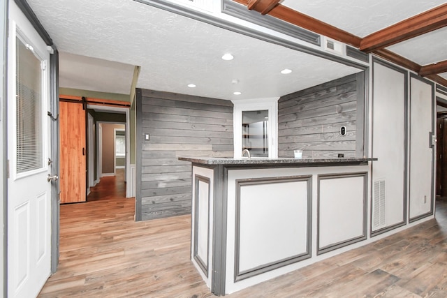 kitchen with wooden walls, light hardwood / wood-style floors, a barn door, and a textured ceiling