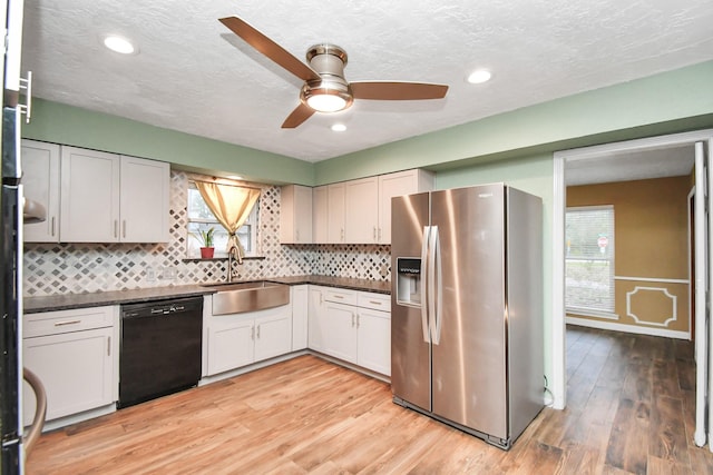 kitchen featuring stainless steel refrigerator with ice dispenser, black dishwasher, sink, and white cabinets