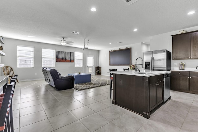 kitchen with sink, a kitchen island with sink, light tile patterned floors, stainless steel appliances, and dark brown cabinets