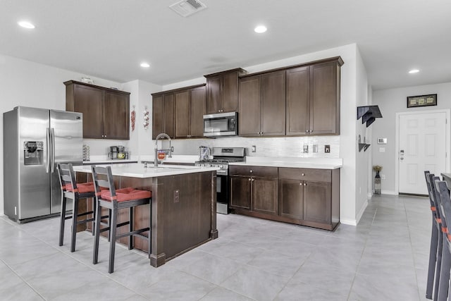 kitchen featuring sink, a breakfast bar area, appliances with stainless steel finishes, a kitchen island with sink, and dark brown cabinets