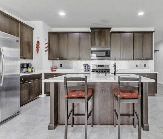 kitchen featuring sink, a breakfast bar, stainless steel appliances, dark brown cabinetry, and a center island with sink