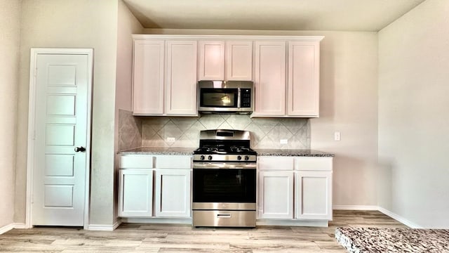 kitchen featuring white cabinetry, stainless steel appliances, stone countertops, and light hardwood / wood-style flooring