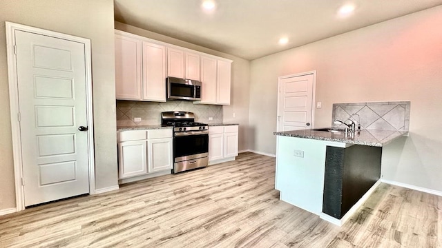 kitchen with sink, light hardwood / wood-style flooring, white cabinetry, stainless steel appliances, and kitchen peninsula