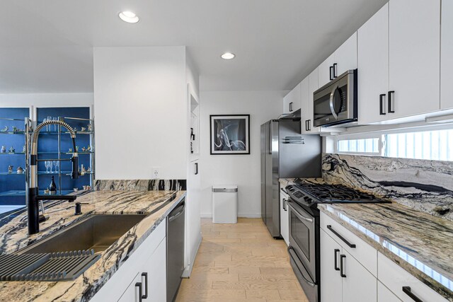 kitchen with appliances with stainless steel finishes, sink, white cabinets, and light stone counters