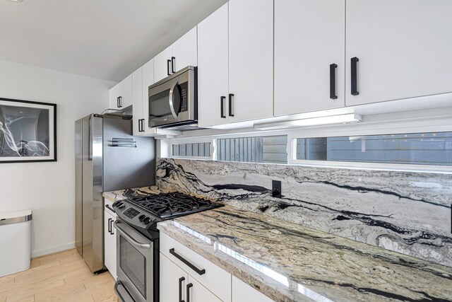 kitchen featuring appliances with stainless steel finishes, light stone countertops, light wood-type flooring, and white cabinets