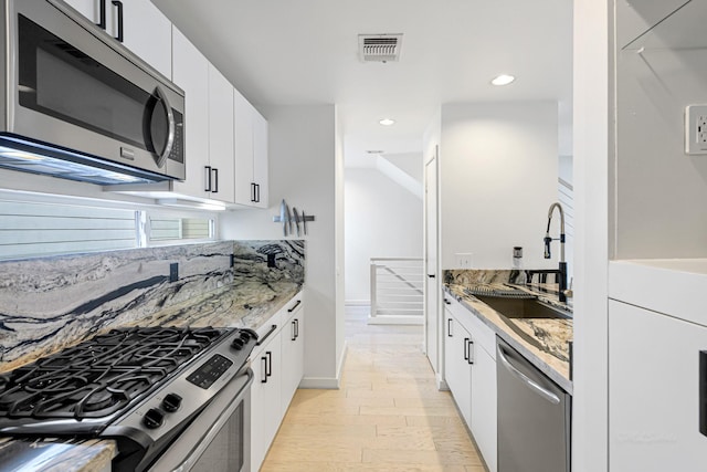 kitchen with sink, appliances with stainless steel finishes, white cabinetry, light stone counters, and light hardwood / wood-style floors