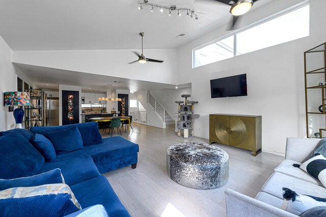 living room with ceiling fan, rail lighting, high vaulted ceiling, and light hardwood / wood-style flooring