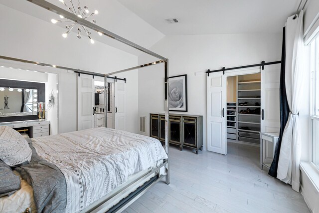 bedroom featuring lofted ceiling, a walk in closet, a notable chandelier, a barn door, and light hardwood / wood-style flooring