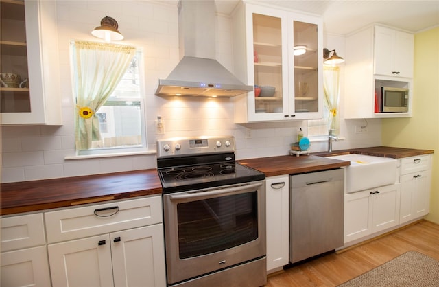 kitchen with sink, butcher block counters, stainless steel appliances, wall chimney range hood, and light wood-type flooring