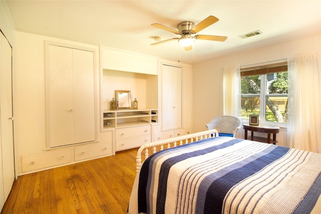 bedroom featuring ceiling fan, light hardwood / wood-style flooring, and two closets