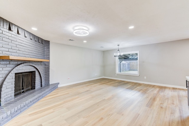 unfurnished living room featuring an inviting chandelier, a brick fireplace, light hardwood / wood-style floors, and a textured ceiling