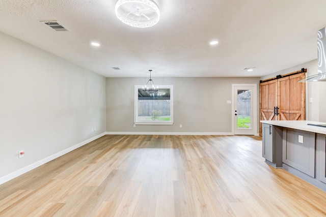 kitchen featuring a textured ceiling, light wood-type flooring, a notable chandelier, pendant lighting, and a barn door