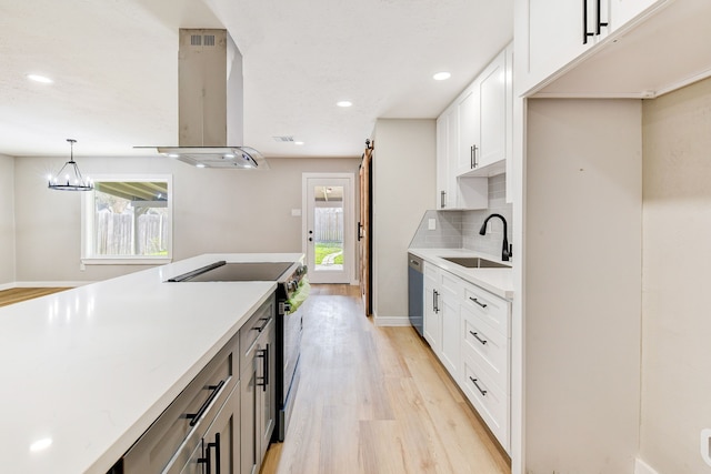 kitchen with sink, wall chimney range hood, appliances with stainless steel finishes, white cabinetry, and decorative light fixtures