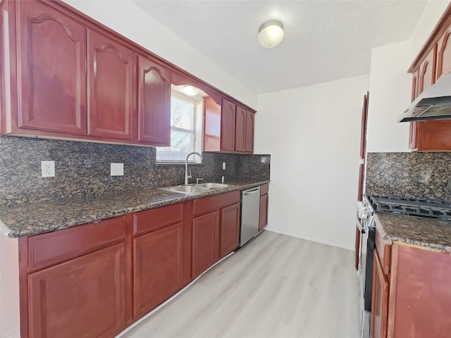 kitchen featuring sink, light hardwood / wood-style flooring, dark stone countertops, stainless steel appliances, and decorative backsplash