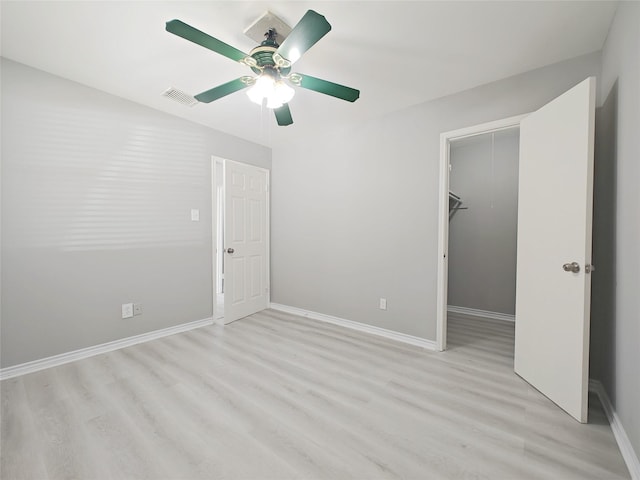 unfurnished bedroom featuring ceiling fan, a spacious closet, light wood-type flooring, and a closet