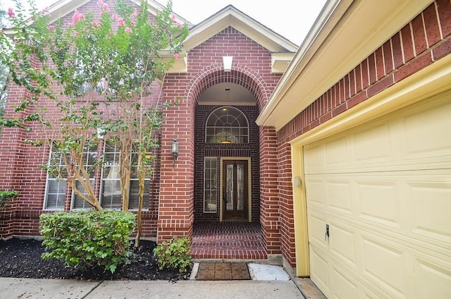 view of exterior entry featuring an attached garage and brick siding