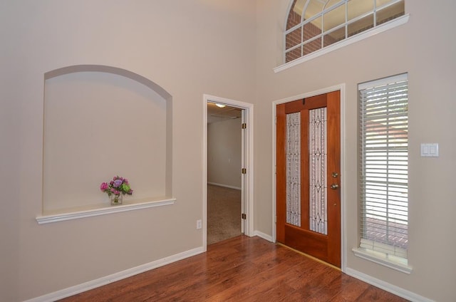 foyer entrance featuring a towering ceiling, baseboards, and wood finished floors