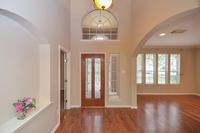 entryway with baseboards, arched walkways, a towering ceiling, wood finished floors, and crown molding