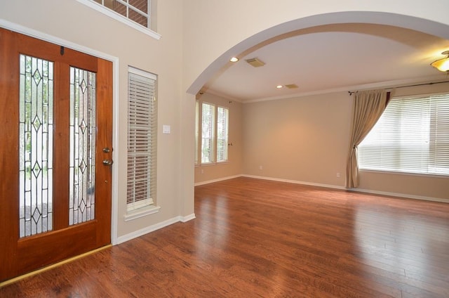 foyer entrance featuring ornamental molding, arched walkways, baseboards, and wood finished floors