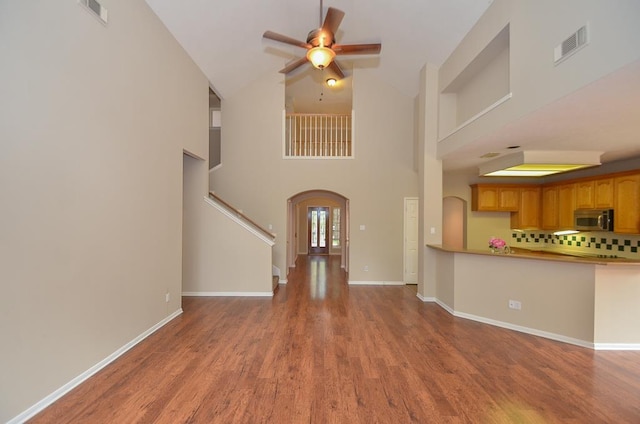 unfurnished living room with arched walkways, wood finished floors, visible vents, a ceiling fan, and stairway