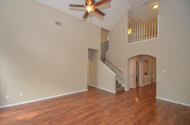 unfurnished living room featuring dark wood-style floors, arched walkways, visible vents, stairway, and ceiling fan